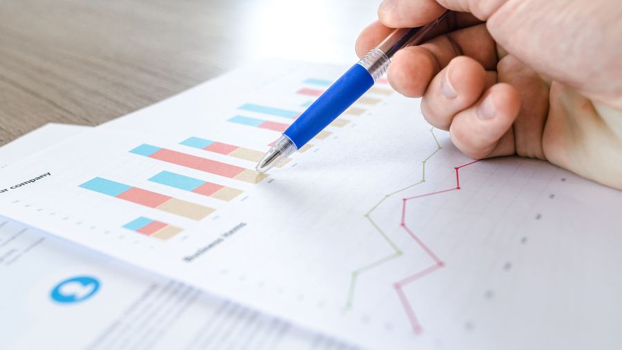 A hand reviewing a printed report with bar charts and trend lines